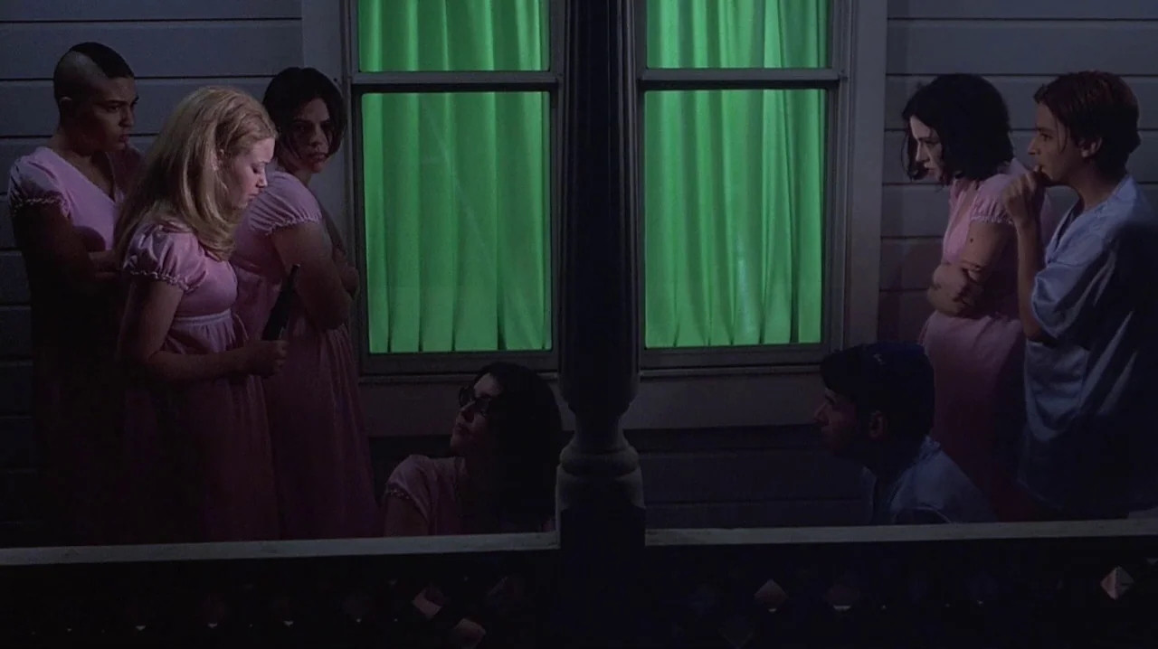 But I’m A Cheerleader (1999) movie still: wide — A group of six people stand on a dark, wooden front porch at night. The interior of the house glows…