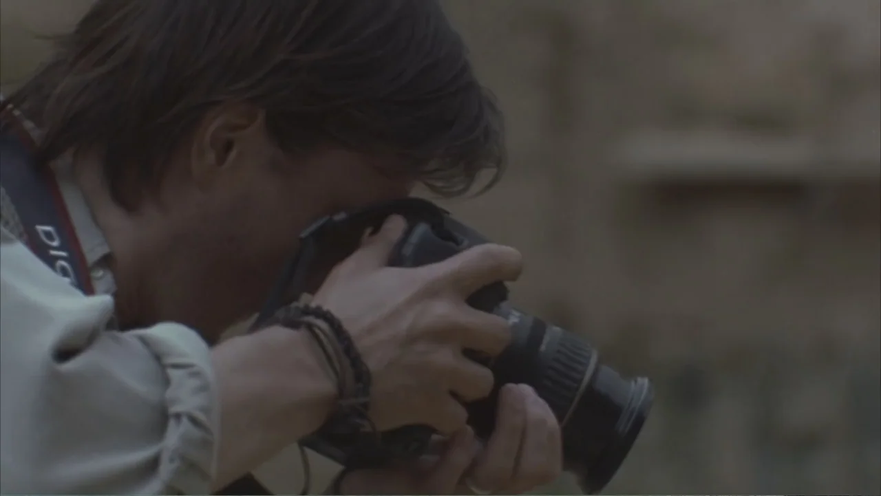A Distant Place (2020) movie still: medium — An outdoor area with a blurred, neutral-toned background of earth and stone. A man in a light-colored…