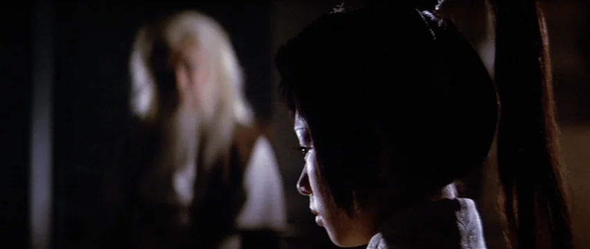 Lone Wolf and Cub: White Heaven in Hell (1974) movie still: medium — A dark, minimally lit interior space contains two individuals facing each…