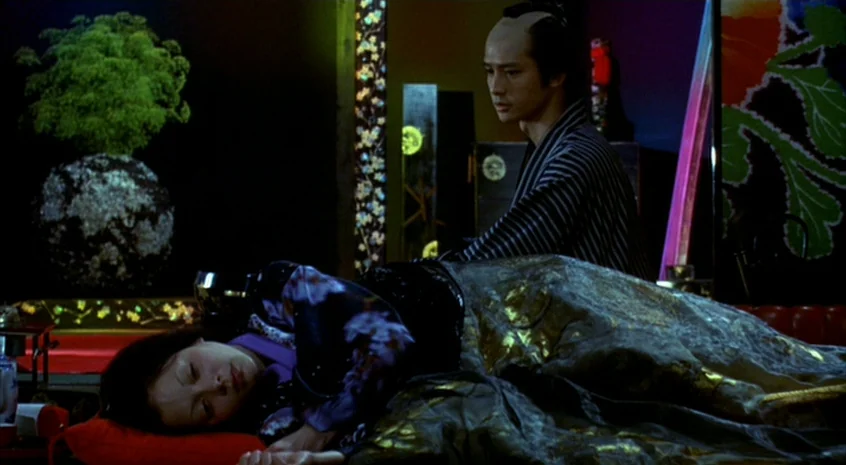 Sakuran (2006) movie still: medium — A dimly lit room with elaborate folding screens and a lush, decorative textile backdrop. A man in a striped…