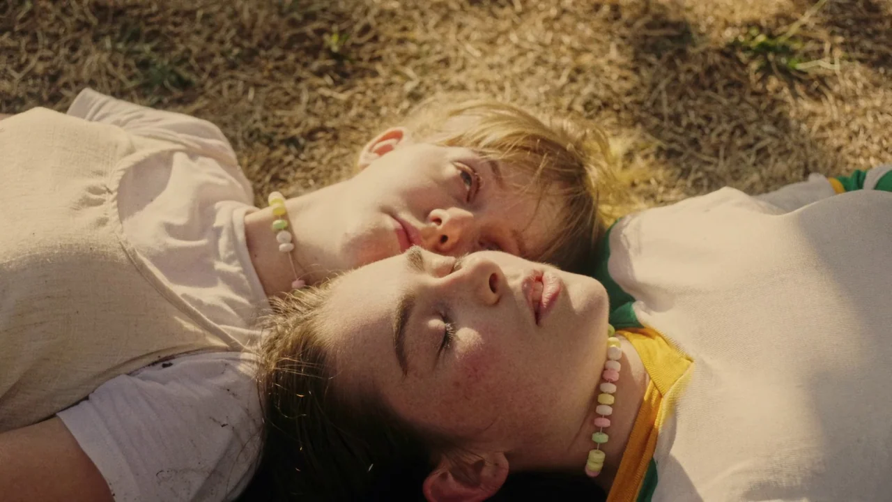 My First Summer (2020) movie still: closeup — Two girls lie on dry, sun-bleached grass under natural daylight. The subjects rest side-by-side with…