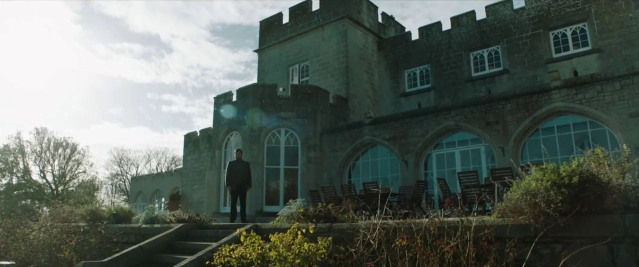 Happy New Year, Colin Burstead (2018) movie still: wide — A stone building with crenelated towers and arched glass doors sits on a lawn. A lone man…