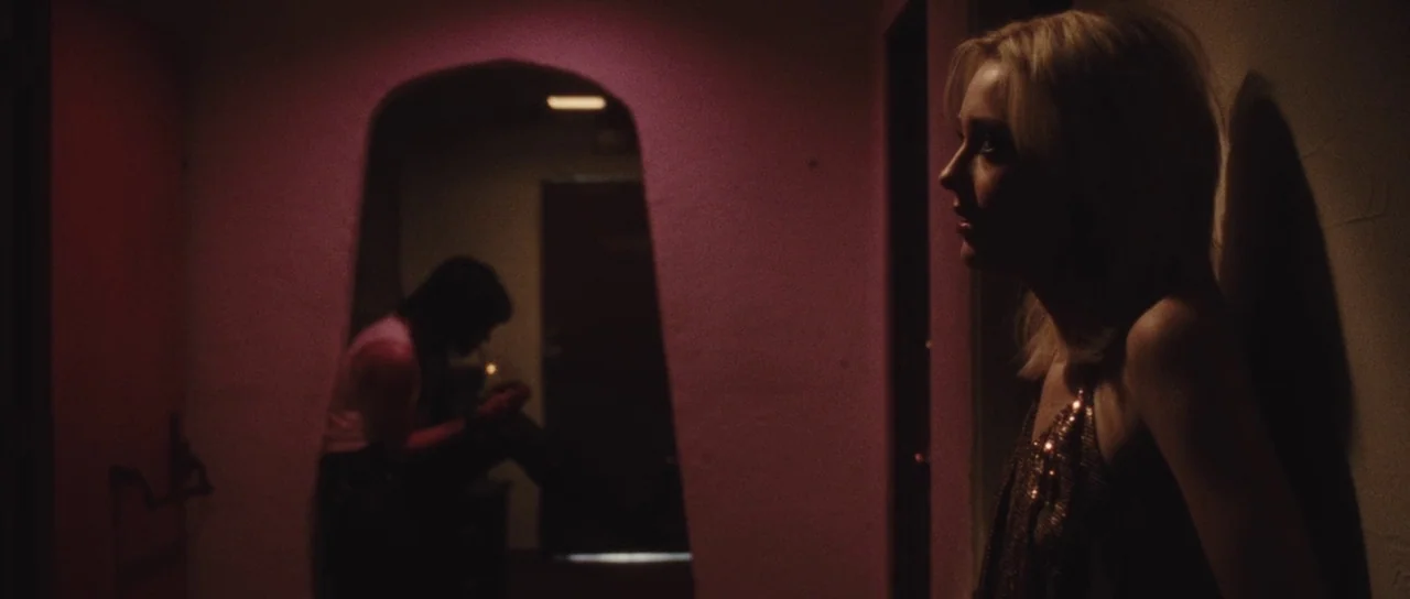 The Runaways (2010) movie still: medium — A dimly lit motel corridor is washed in heavy red light from a doorway. A blonde woman stands in the…