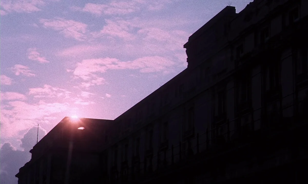 Daughters of Darkness (1971) movie still: establishing — A dark, silhouetted building stands against a bright, purple-hued evening sky. The setting…