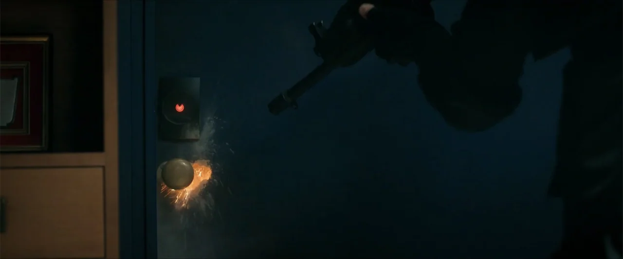 Checkmate (2015) movie still: medium — A dark interior hallway shows a door with a glowing red electronic lock panel. A person's hand holds a rifle…