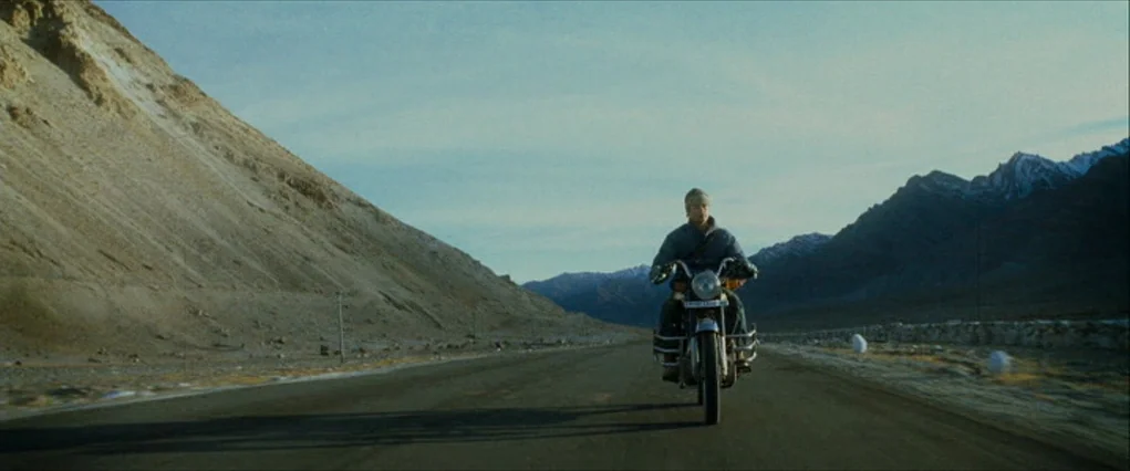 The Curious Case Of Benjamin Button (2008) movie still: wide — A wide paved road stretches through a vast, arid mountain valley with rocky slopes. A…