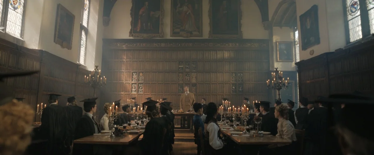Young Sherlock Holmes (1985) movie still: wide — A historic dining hall with dark wood paneling and large oil paintings on walls. Students in formal…