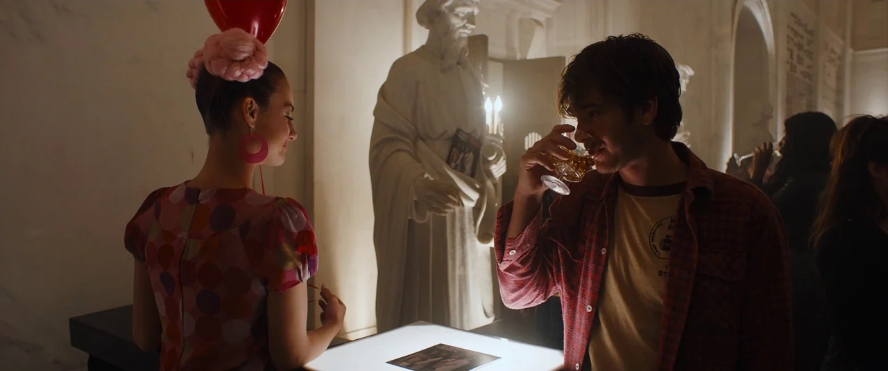 Under The Silver Lake (2018) movie still: medium — A dimly lit museum gallery features marble statues and illuminated displays. A man holding a…