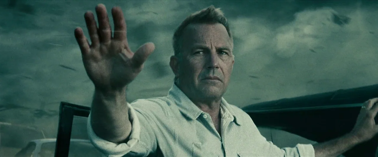Man Of Steel (2013) movie still: medium — A man stands outdoors near a vehicle under a dark, storm-filled sky. He holds his arm and hand forward to…