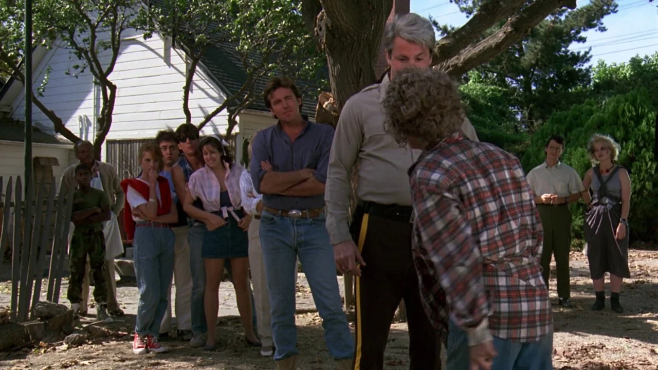 Friday the 13th: A New Beginning (1985) movie still: fullbody — A suburban backyard with a white house and a picket fence in the distance. A group…