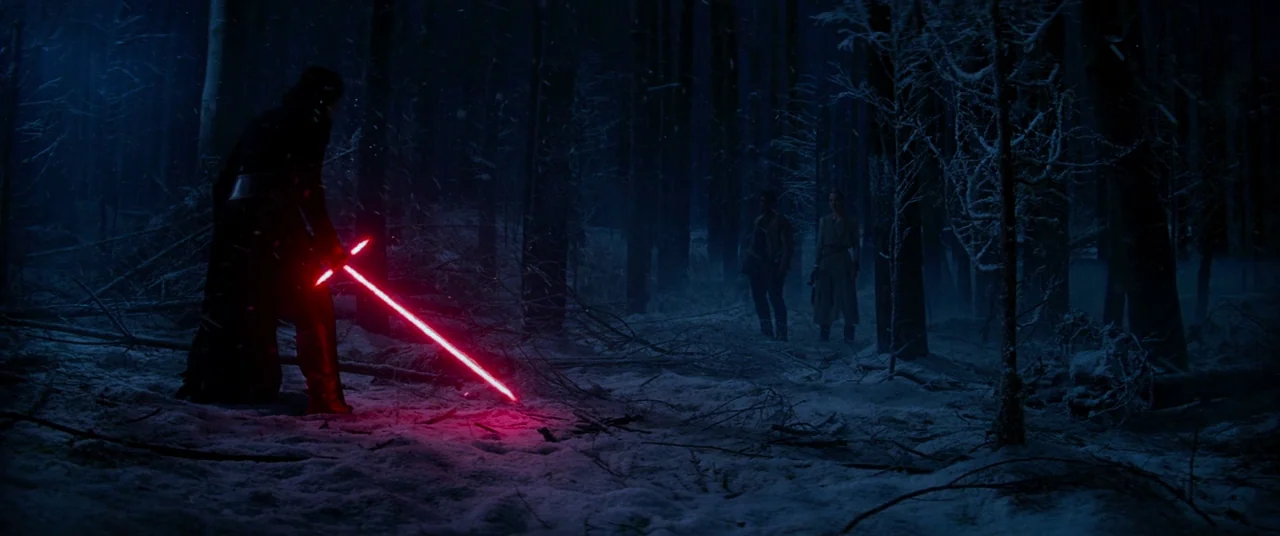 Star Wars: The Force Awakens (2015) movie still: wide — A dense, snow-covered forest at night features tall dark trees and fallen branches. A…