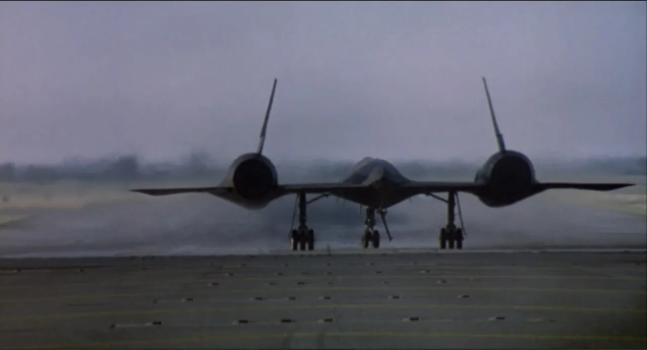 Air Rage (2001) movie still: wide — An asphalt runway extends into the distance under a grey, overcast sky. A Lockheed SR-71 Blackbird aircraft is…