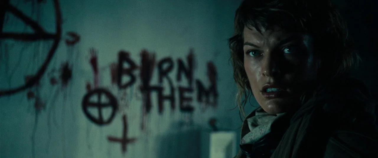 Resident Evil: Extinction (2007) movie still: medium — A dimly lit room with peeling paint and dark symbols written on a wall. A woman with damp…