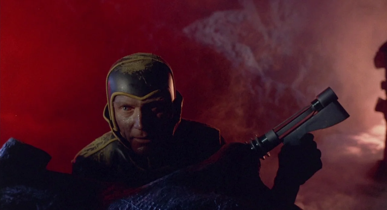 Planet of the Vampires (1965) movie still: medium — A rocky alien terrain is washed in intense red light and swirling smoke clouds. A man wearing a…