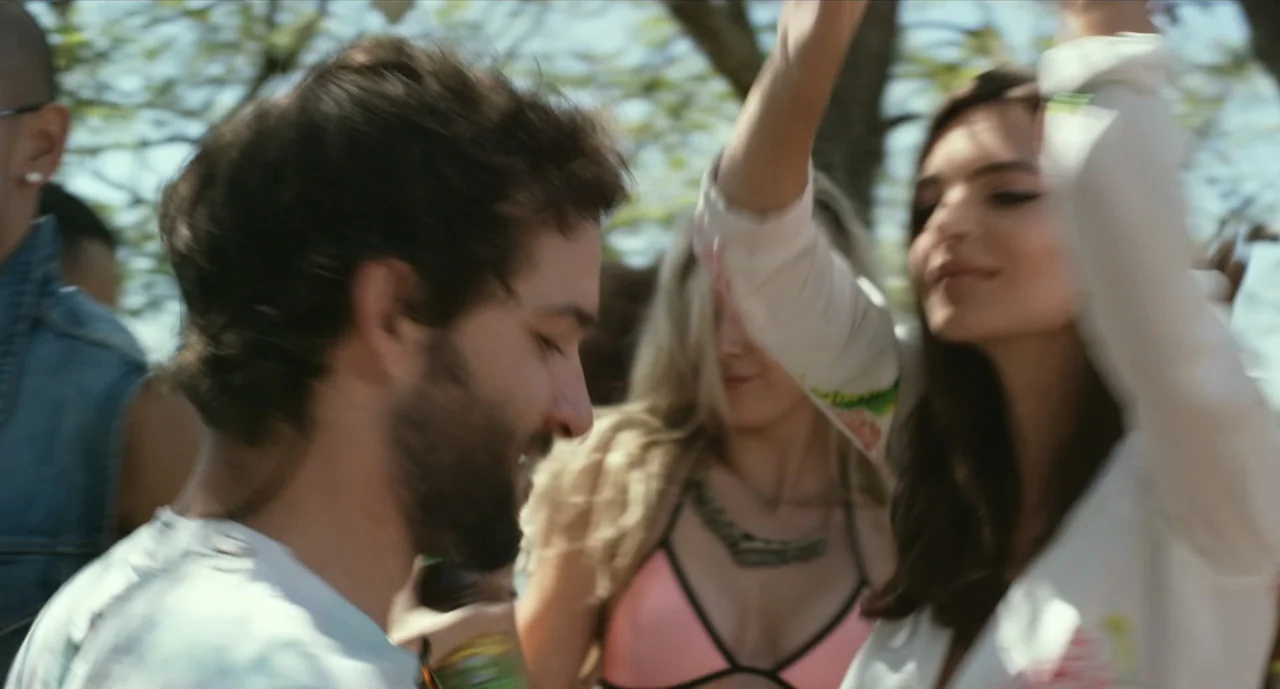 We Are Your Friends (2015) movie still: medium — A sunlit outdoor area features people dancing under trees. A young man and woman stand in the…