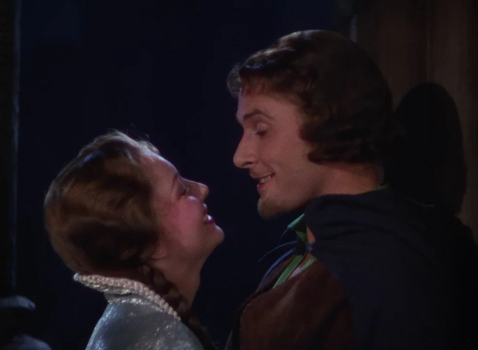 The Adventures of Robin Hood (1938) movie still: medium — A dark indoor space with stone masonry behind a man and woman. They stand close together…