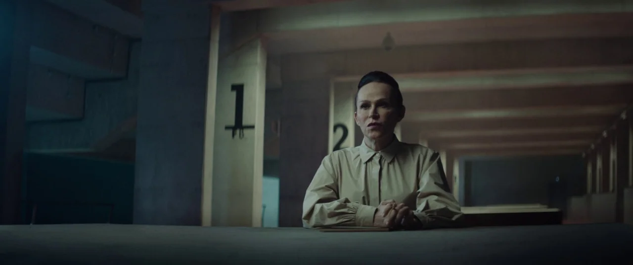 The Platform (2019) movie still: medium — A concrete shooting range features numbered stalls and long, dim, industrial architectural lines. A…