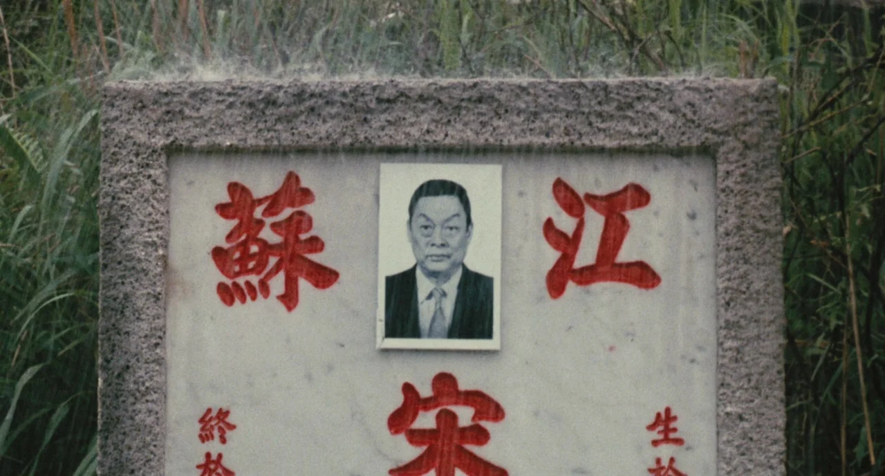 A Better Tomorrow (1986) movie still: closeup — A stone grave marker is situated in a patch of wild, unkempt green grass. A rectangular portrait of…