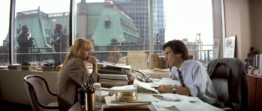 The Big Blue (1988) movie still: medium — A cluttered professional workspace features a large window overlooking a city building terrace. A man and…