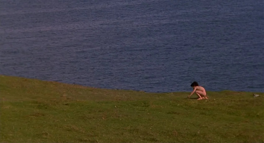 The Secret Of Roan Inish (1994) movie still: wide — A grassy coastal cliff overlooks a dark blue ocean expanse under daylight conditions. A young…