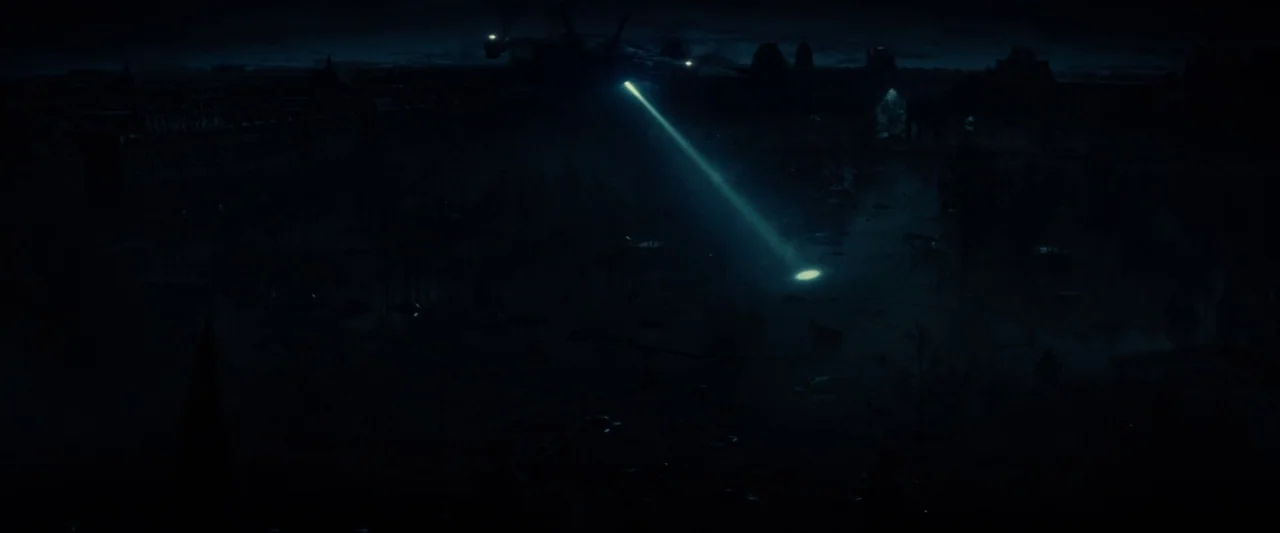 Edge of Tomorrow (2014) movie still: establishing — An aerial night view of a dark plaza with large buildings in the distance. An aircraft hovering…