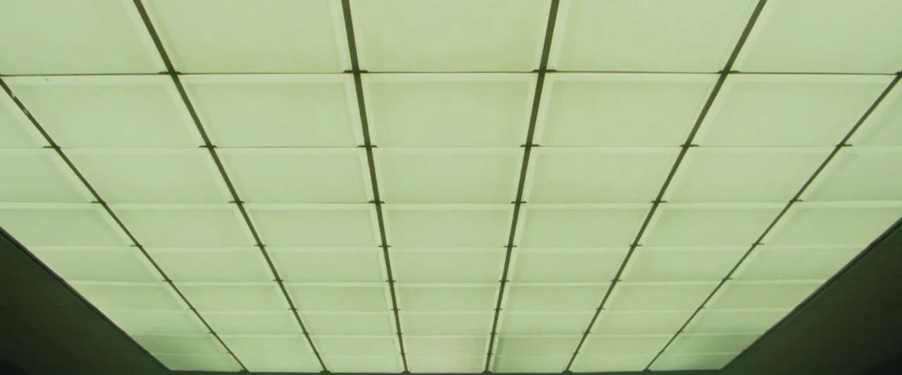 Lost River (2014) movie still: establishing — A ceiling features a grid of illuminated square light panels separated by thin dark frames. The panels…