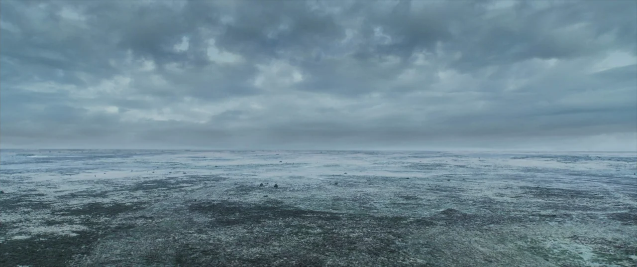 The Promised Land (2023) movie still: establishing — A vast, frozen expanse of tundra stretches toward the horizon under a heavy sky. Dense, grey…