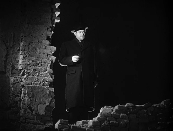 The Third Man (1949) movie still: fullbody — A man stands in the gap of a partially destroyed brick structure at night. He is illuminated by a sharp…
