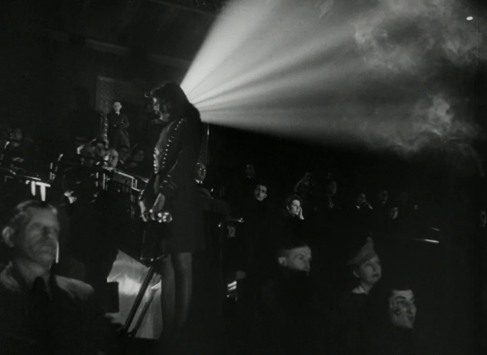 Brief Encounter (1945) movie still: medium — A dark, crowded 1940s cinema with rows of spectators visible in the dim light. A bright beam of light…