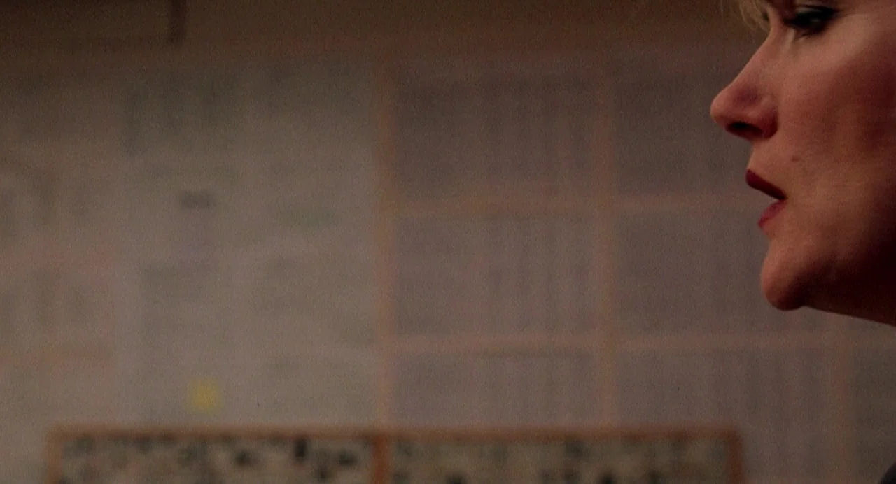 Office Killer (1997) movie still: closeup — An interior office space features a blurred document wall in the background. A woman's profile is…