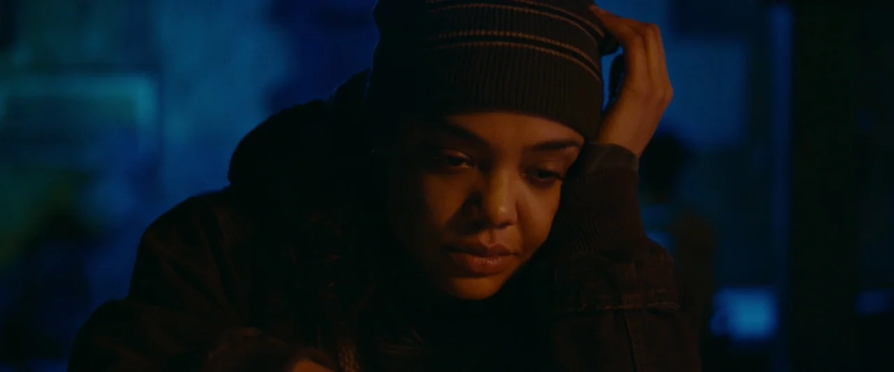 Little Woods (2018) movie still: closeup — A dimly lit interior space with contrasting blue background tones. A young woman rests her chin on her…