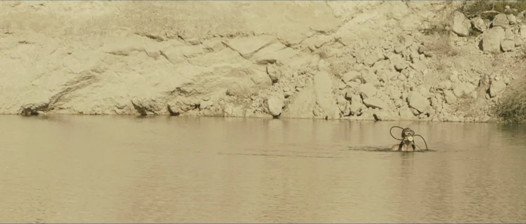 Lasting (Nieulotne) (2013) movie still: wide — A man wearing scuba gear floats in a large, calm quarry lake. A steep, rocky cliff wall forms the…