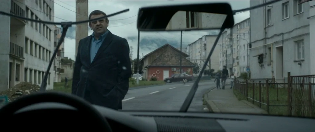 Graduation (2016) movie still: medium — An overcast urban setting features rows of multi-story concrete residential apartment blocks. A middle-aged…