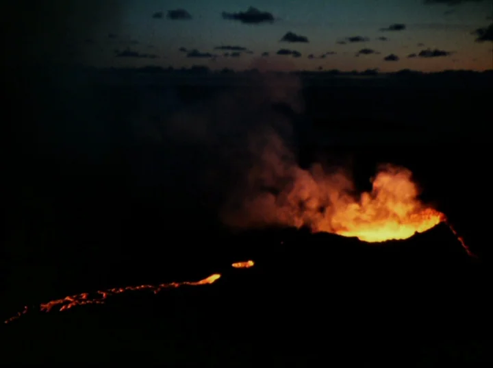 Lucifer Rising (1972) movie still: establishing — A dark volcanic landscape at night showing a crater emitting bright orange glowing lava. Plumes of…