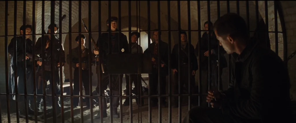 Inglourious Basterds (2009) movie still: wide — A dimly lit brick bunker interior features a heavy metal bar divider. A group of armed soldiers…
