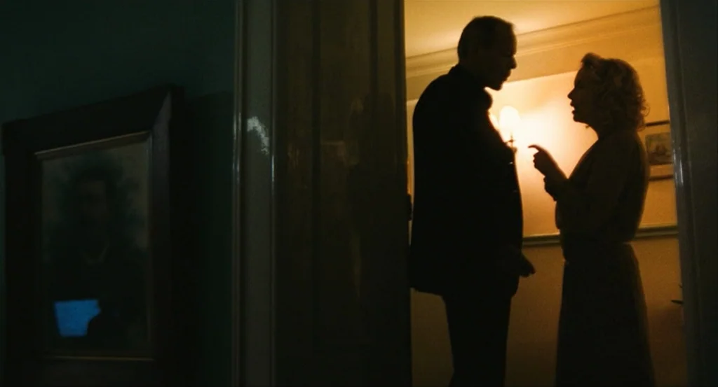This Night (2008) movie still: medium — A dimly lit passage leads into a brightly lit room. A man and a woman stand within the threshold conversing.