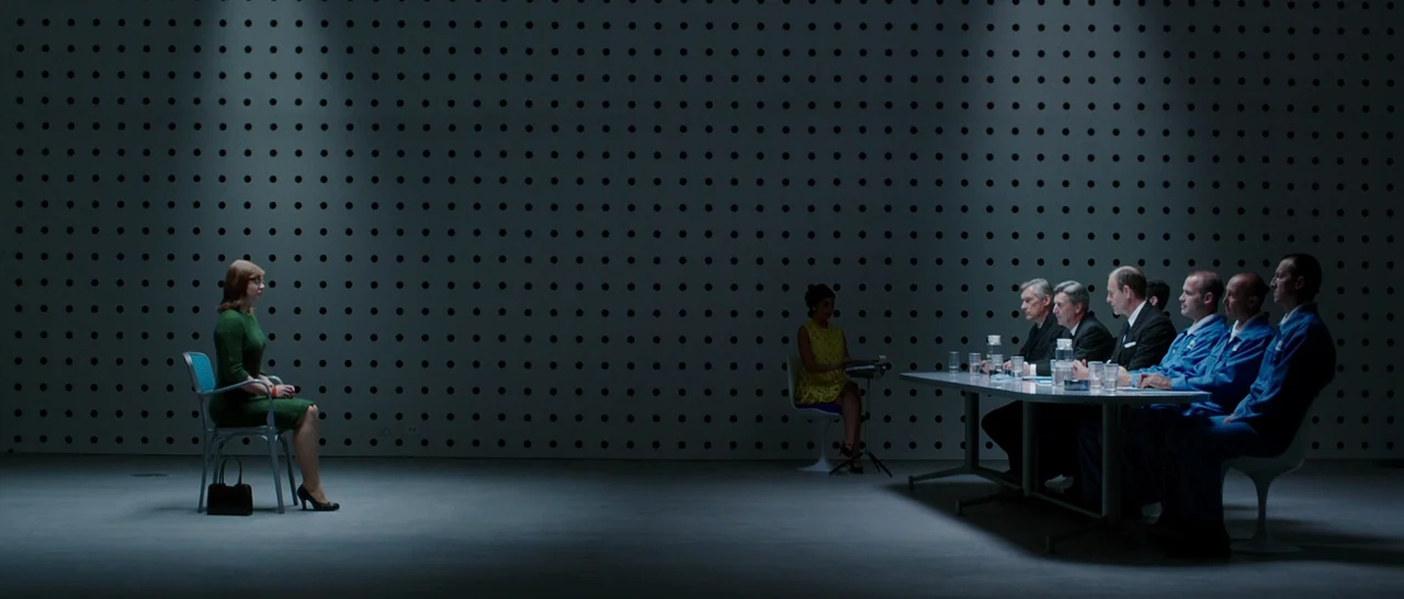 Predestination (2014) movie still: wide — A minimalist interrogation space features a grid-patterned wall with dark, circular accents throughout. A…