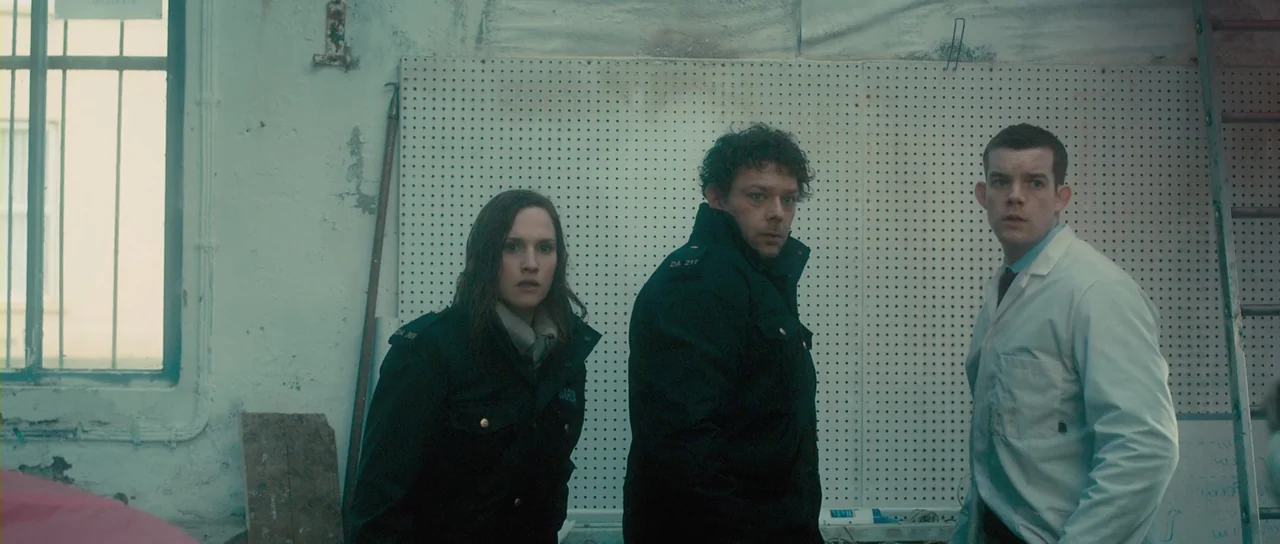 Grabbers (2012) movie still: medium — A workshop interior features a white pegboard wall and a large metal-framed window. Three individuals in…