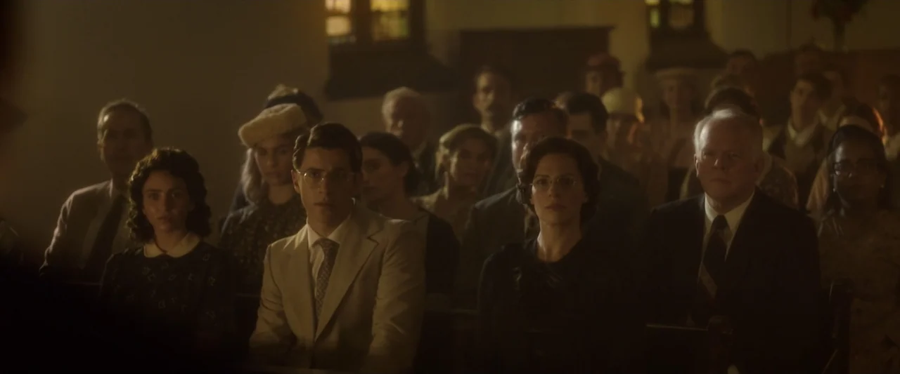 Reagan (2024) movie still: medium — A group of people sits together in a dimly lit, wood-paneled room. The individuals are dressed in 1940s-style…