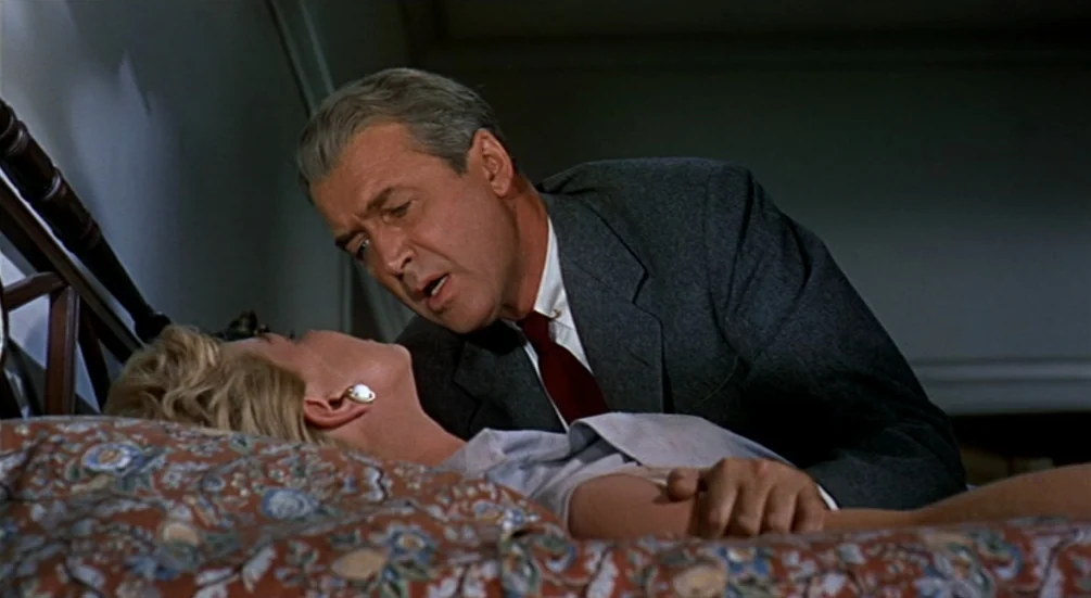 The Man Who Knew Too Much (1956) movie still: medium — A dimly lit bedroom features a floral patterned bedspread and dark, shadow-filled walls. A…