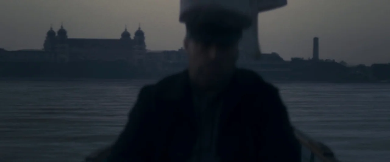 The Immigrant (2013) movie still: medium — A man stands on a boat while traveling across a body of water. Ellis Island with its prominent twin domes…