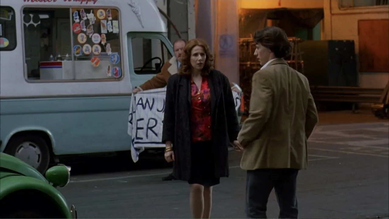Starter for 10 (2006) movie still: fullbody — An asphalt parking lot features an ice cream van parked in the background. A woman and a young man…