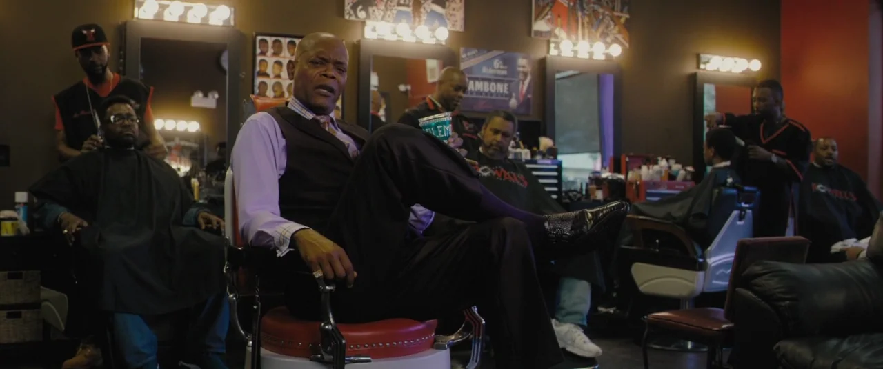 Chi-raq (2015) movie still: medium — A bustling urban shop filled with mirrors and vintage red chairs for grooming clients. A man in a vest occupies…
