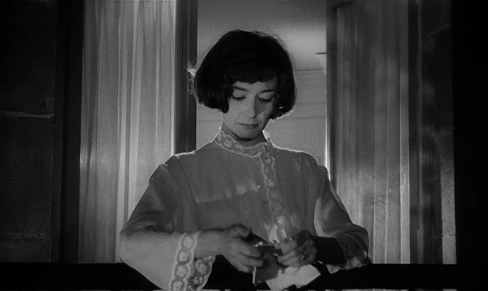 Thérèse Desqueyroux (1962) movie still: medium — A woman stands on a balcony at night with sheer curtains behind her. She looks down while holding a…