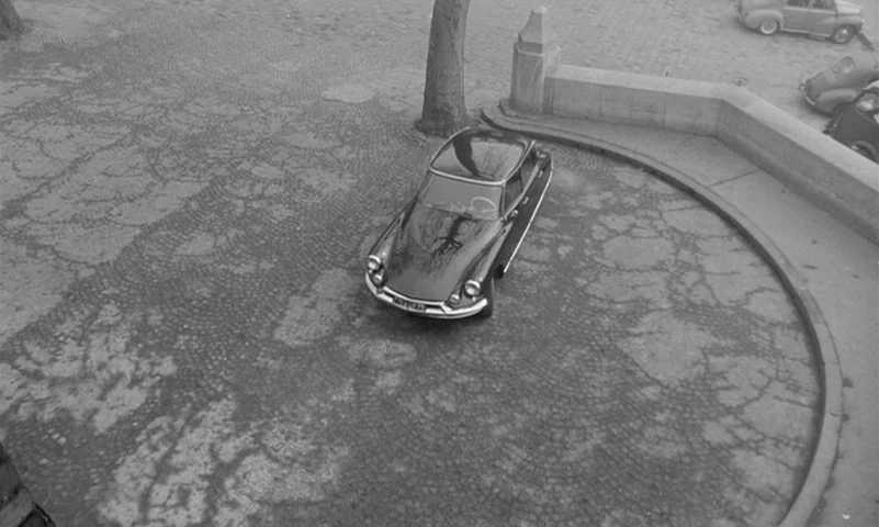 Eyes Without A Face (1960) movie still: wide — A dark Citroen DS is parked on a curved cobblestone section near a low wall. A bare tree trunk stands…