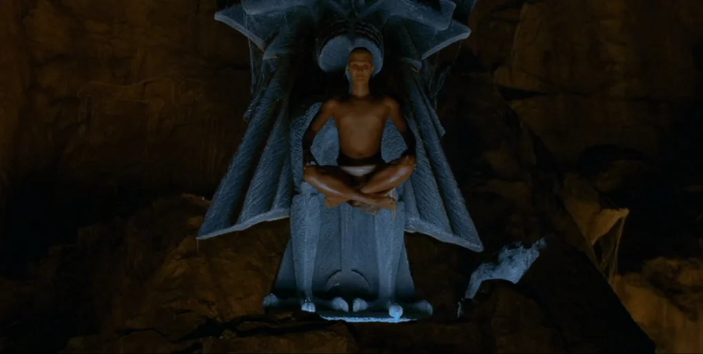 Dominion: Prequel to the Exorcist (2005) movie still: medium — A dark, textured cave interior contains a large, elaborate stone throne carved from…