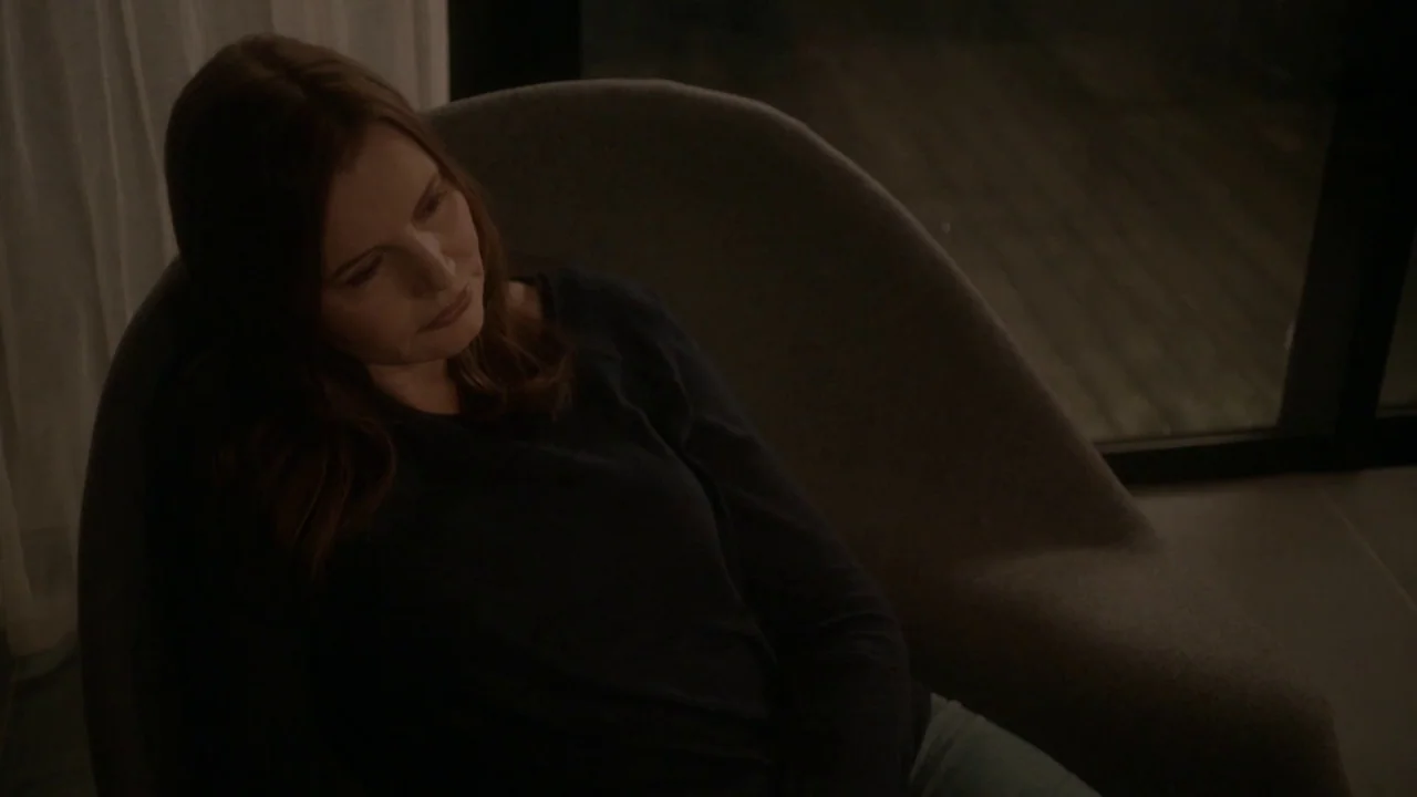 Marjorie Prime (2017) movie still: medium — A dimly lit modern room features a large gray upholstered chair. A woman sits in the chair while looking…