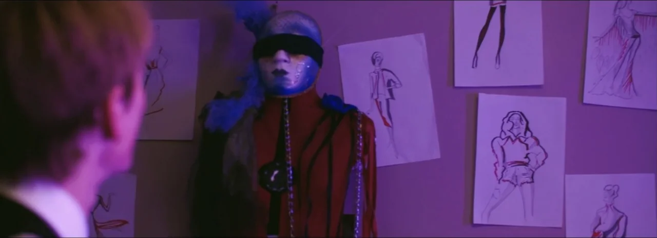 DannyBoy (2020) movie still: medium — A wall is covered with various fashion sketches pinned to a purple surface. A person stands before a mannequin…