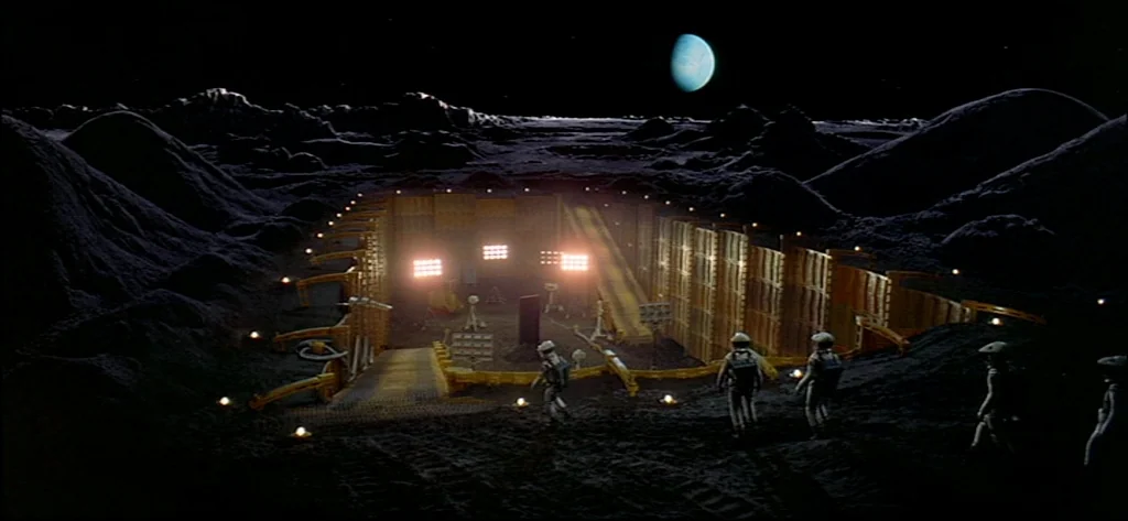 2001: A Space Odyssey (1968) movie still: wide — A lunar excavation site features a deep rectangular pit illuminated by numerous bright floodlights.…