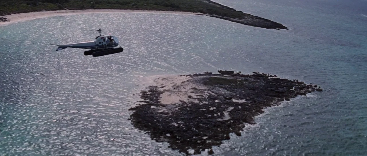 Thunderball (1965) movie still: establishing — A small helicopter glides over shallow coastal waters and a rocky outcrop. Sparse green vegetation…